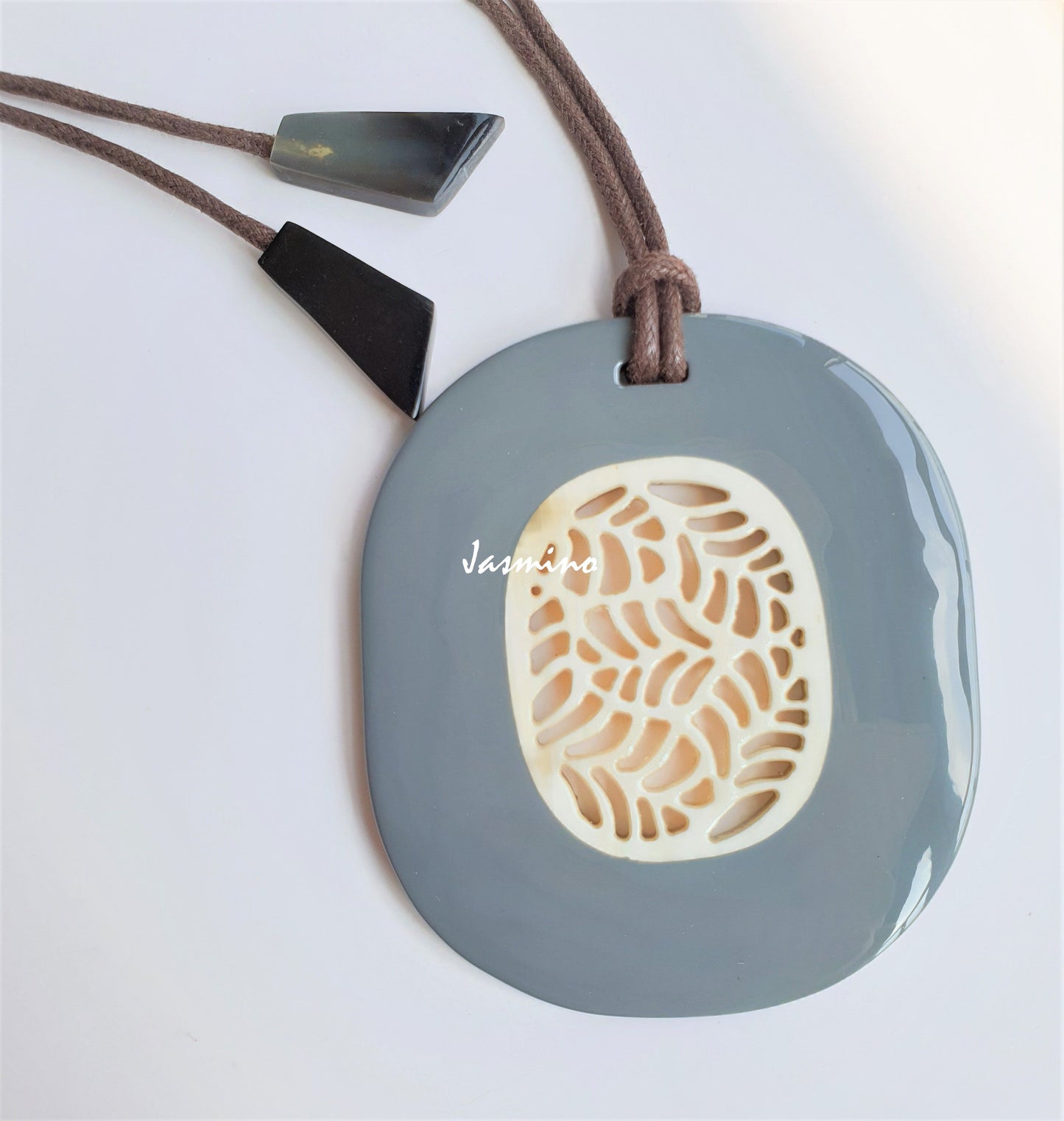 unique handmade oval pendant features greyish blue outline that has a central white flower shape in natural buffalo horn 