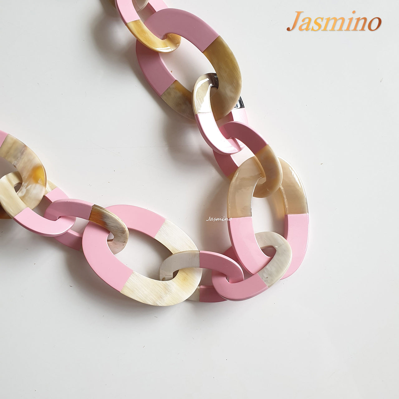 A wide chain necklace features rose pink and natural buffalo horn on a white background