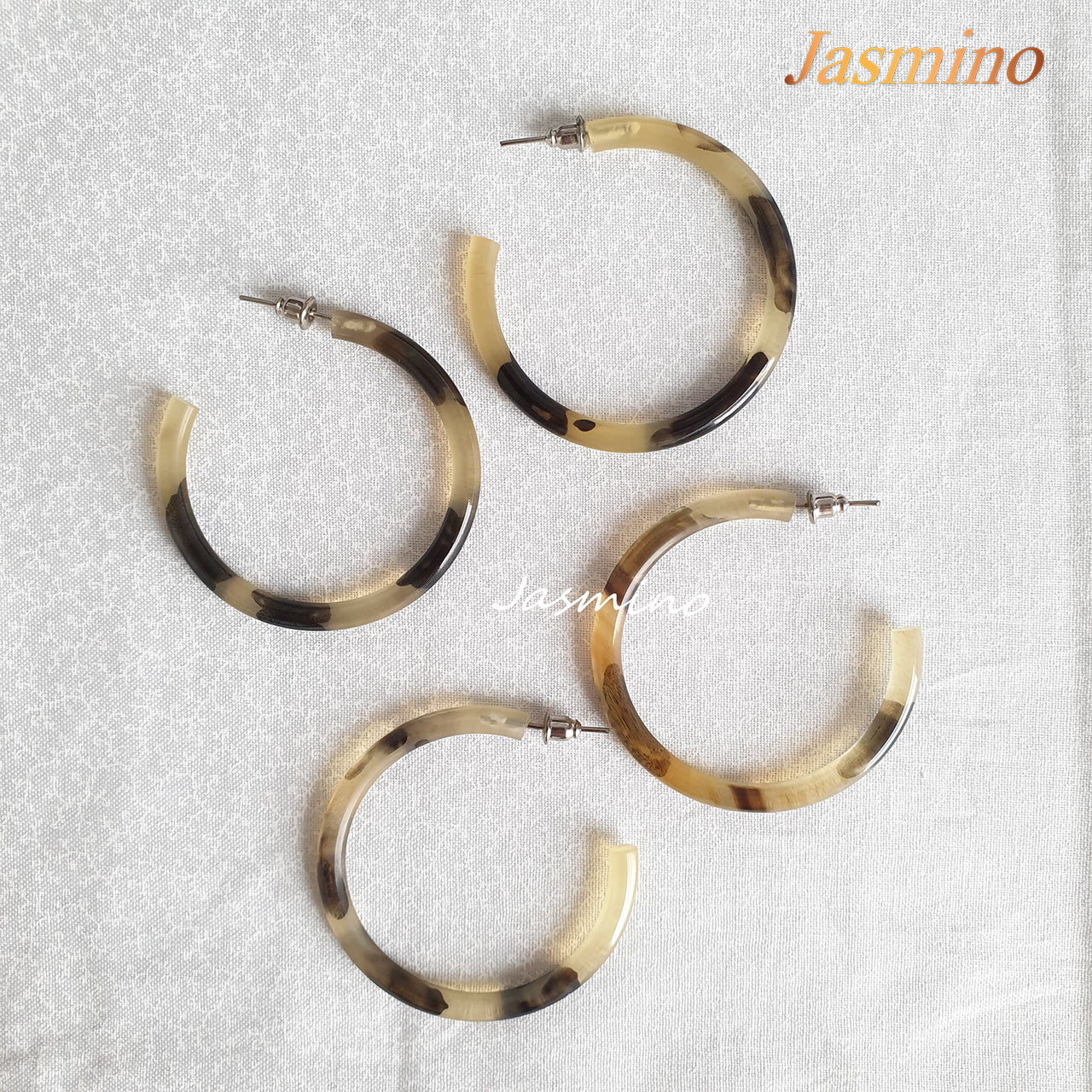 Handmade C-shaped hoop earrings feature a mix of brown and yellow color and natural horn on the light background