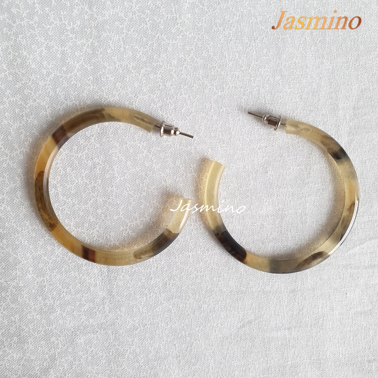 Handmade C-shaped hoop earrings feature a mix of brown and yellow color and natural horn on the light background