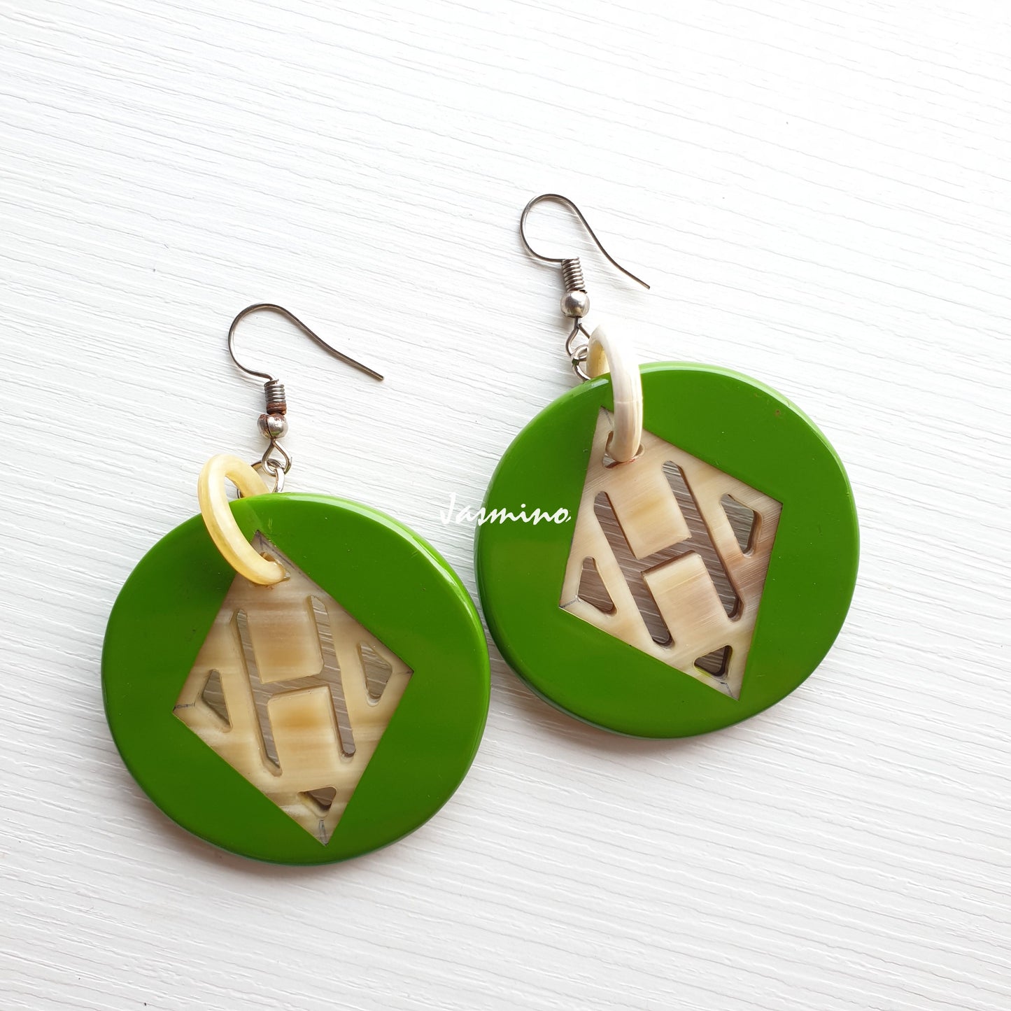 Handmade dangle earrings feature green and a circular shape in the natural light