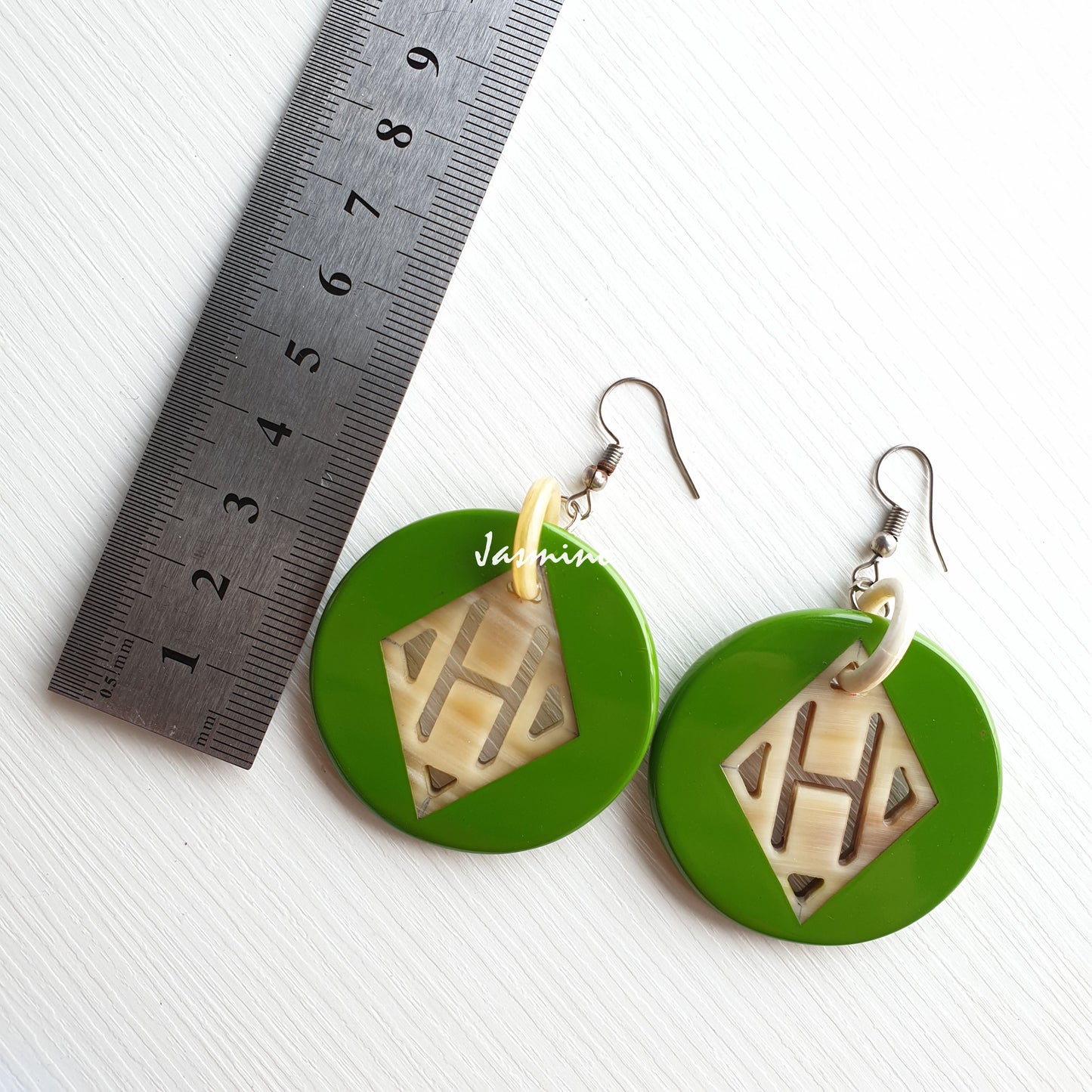 Handmade dangle earrings feature green and a circular shape in the natural light