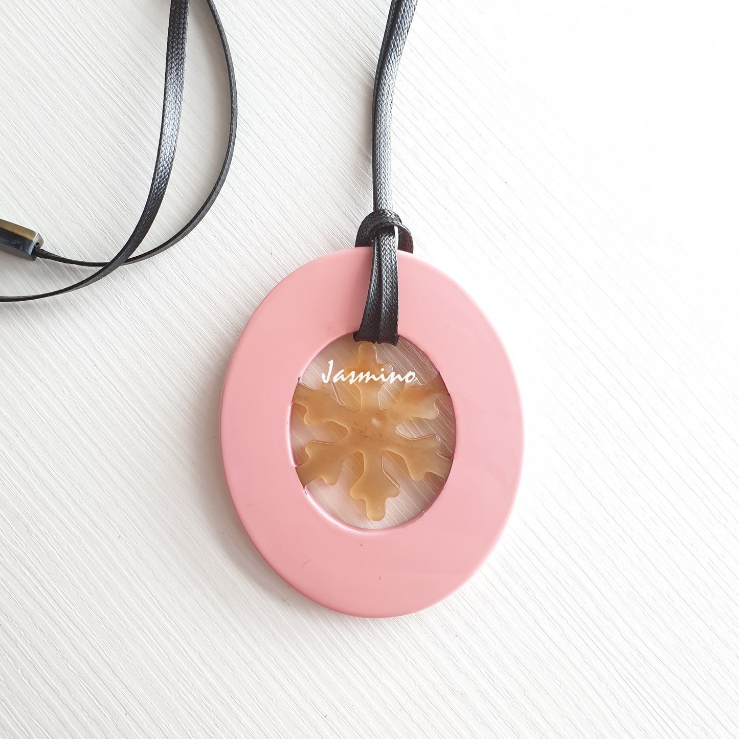 Elliptical coral pink pendant with snowflake pattern inside on the light background, impressive Christmas gift for her