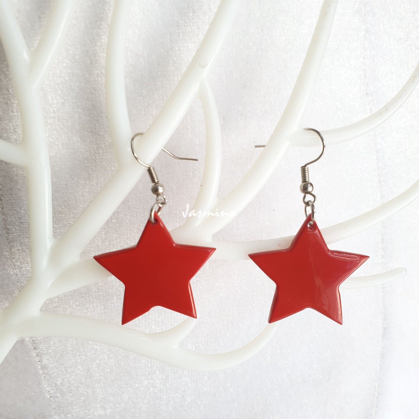 Handmade dangle earrings are detailed by a star shape and red colour on white faux branches 