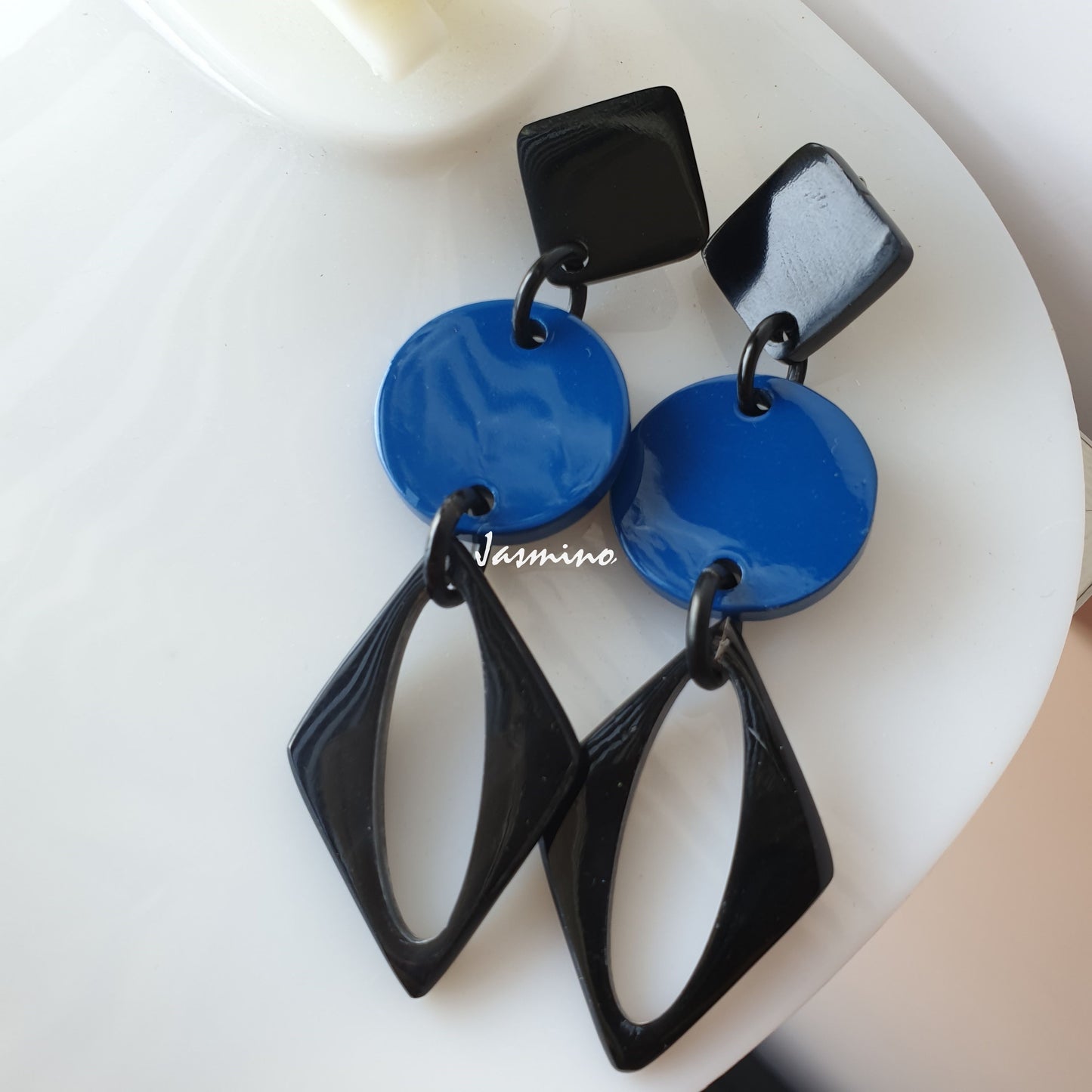 A pair of handmade drop earrings feature black and blue color in the natural light