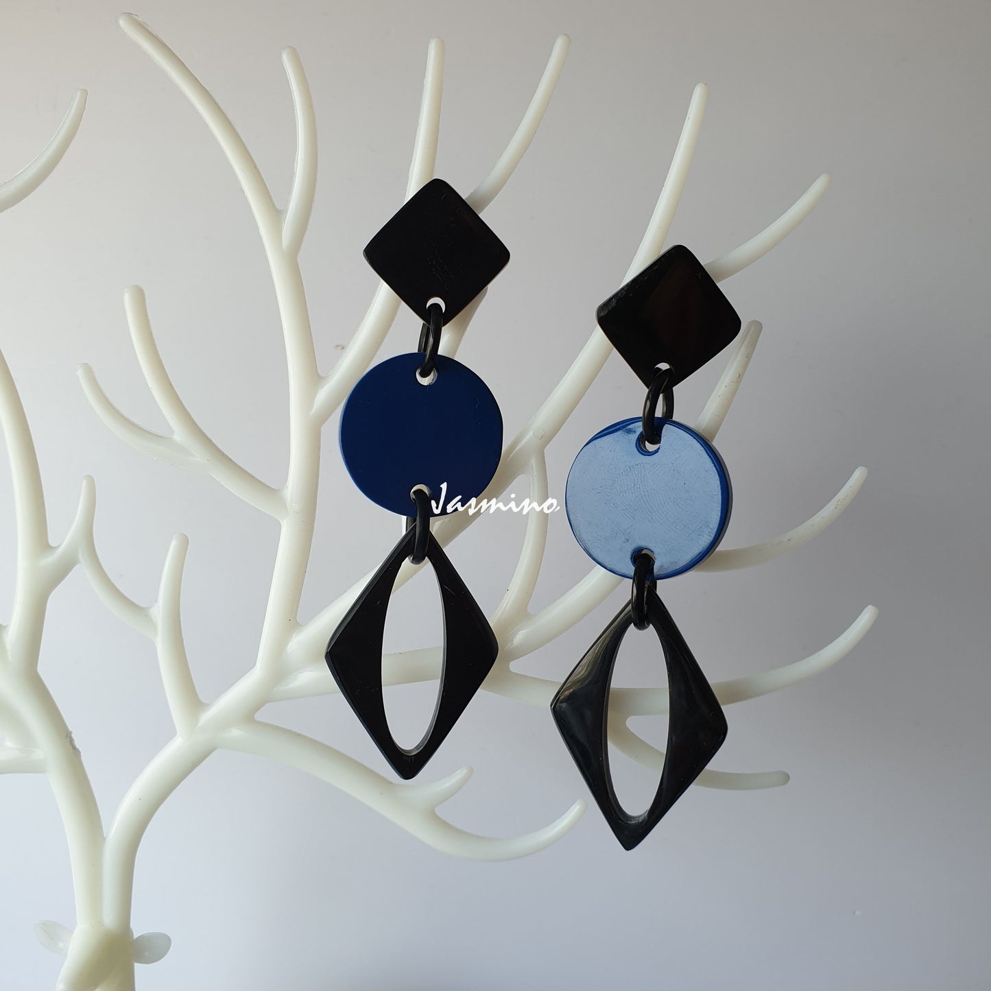 A pair of handmade drop earrings feature black and blue color on white faux branches