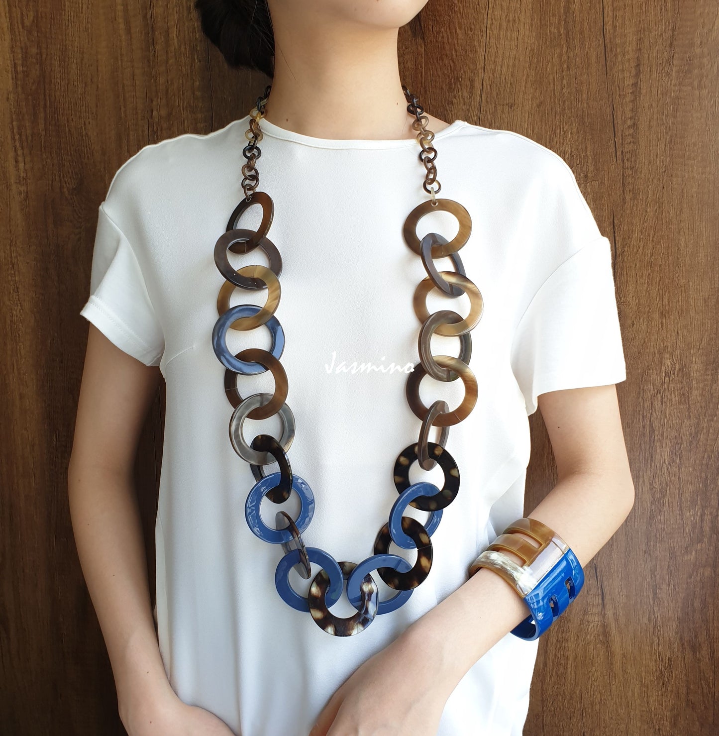 A model is wearing blue necklace made from a series of lacquered circular horn linked on a light background, an impressive gift for her