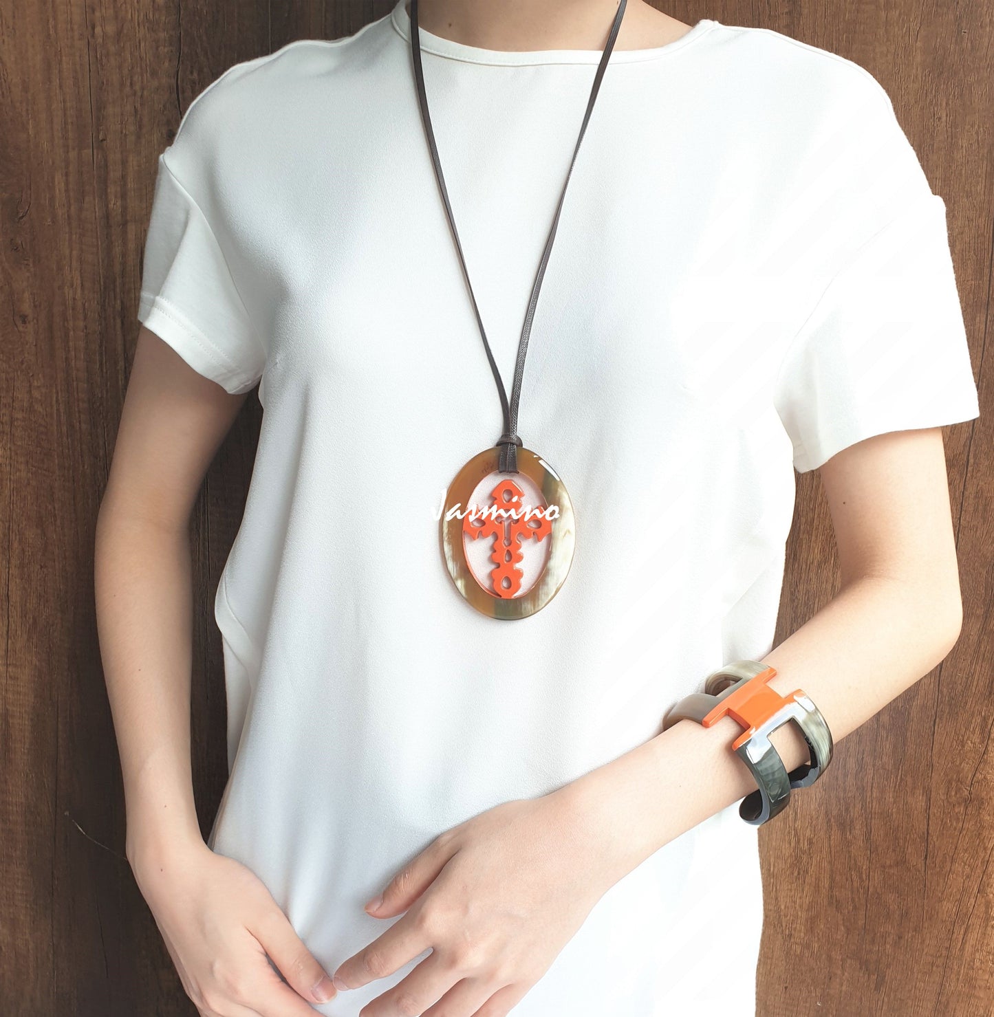 A model is wearing Jasmino unique handmade cross oval pendant in natural buffalo horn and orange for men and women