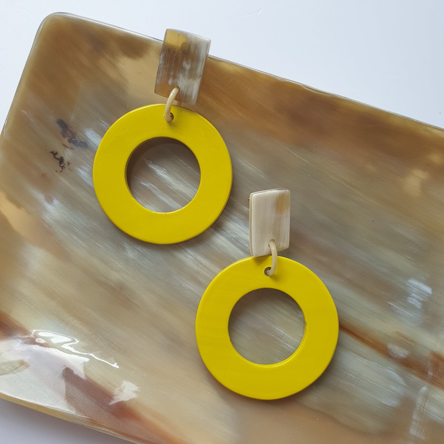 Handmade circle drop earrings are covered by yellow and made by natural buffalo horn on a table in the natural light