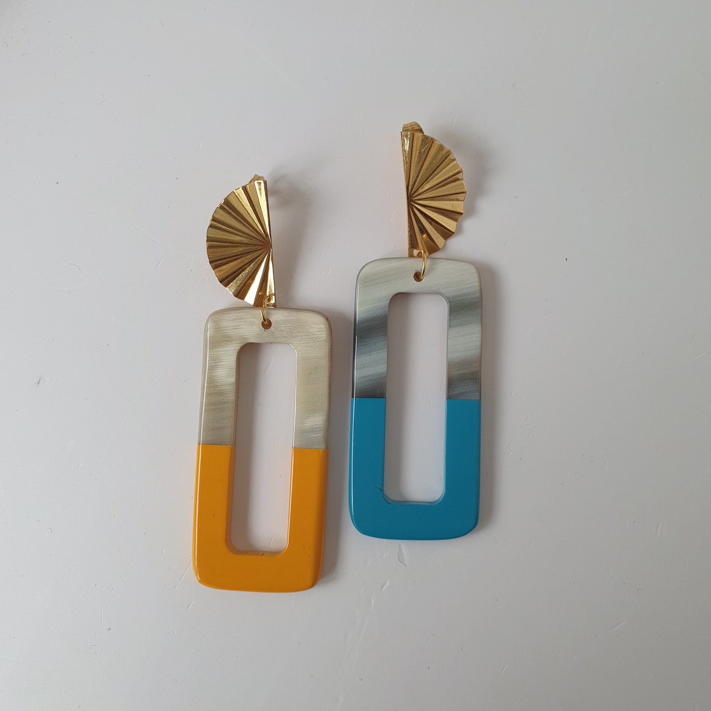 Two handmade natural buffalo horn earrings while the yellow earring is on the left and the turquoise earring is on the right on a light background