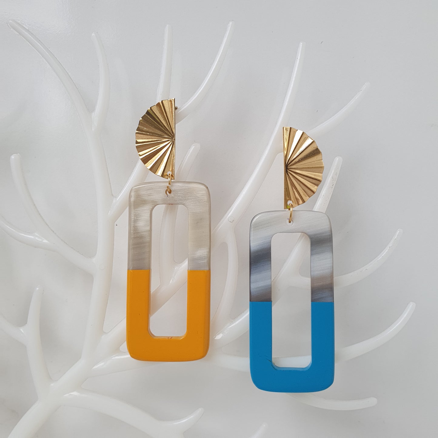 Two handmade natural buffalo horn earrings while the yellow earring is on the left and the turquoise earring is on the right on faux branches